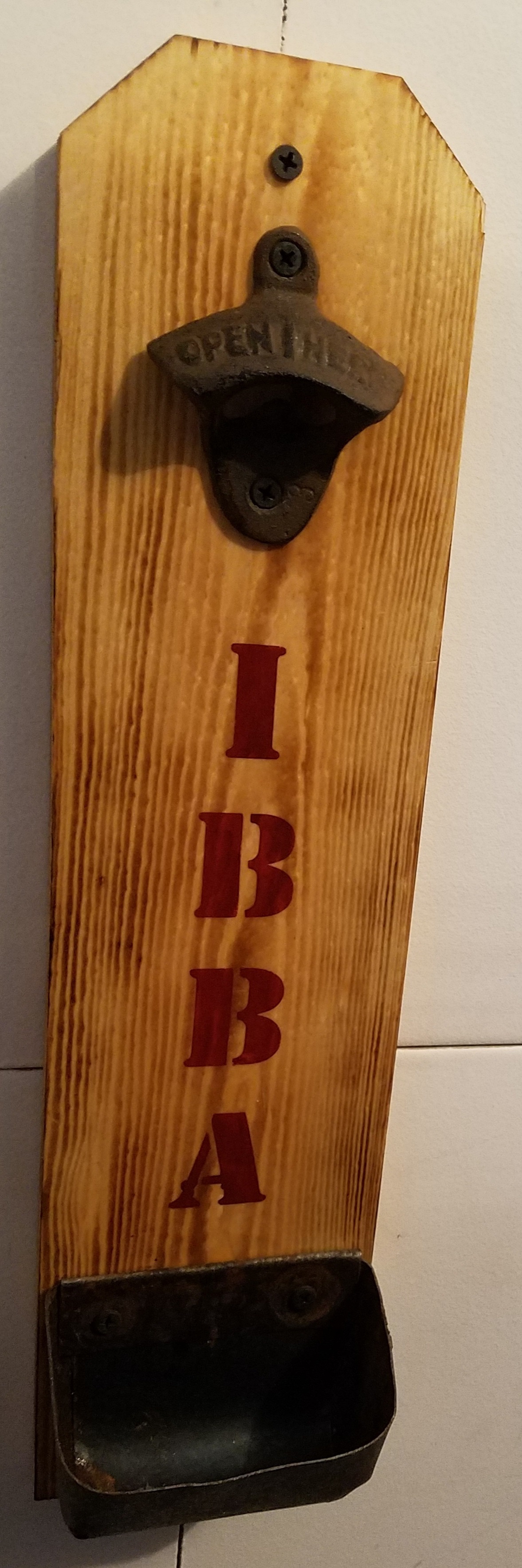 Picture of bottle opener and bottle caps tray nailed on a piece of wood. The piece of wood is customized with a logo.